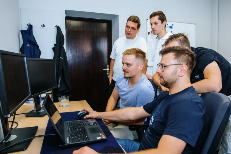 MES optymalizacja produkcji (5 programistów – dwaj siedza przed komputerami, przy biurku, trzech stoi)