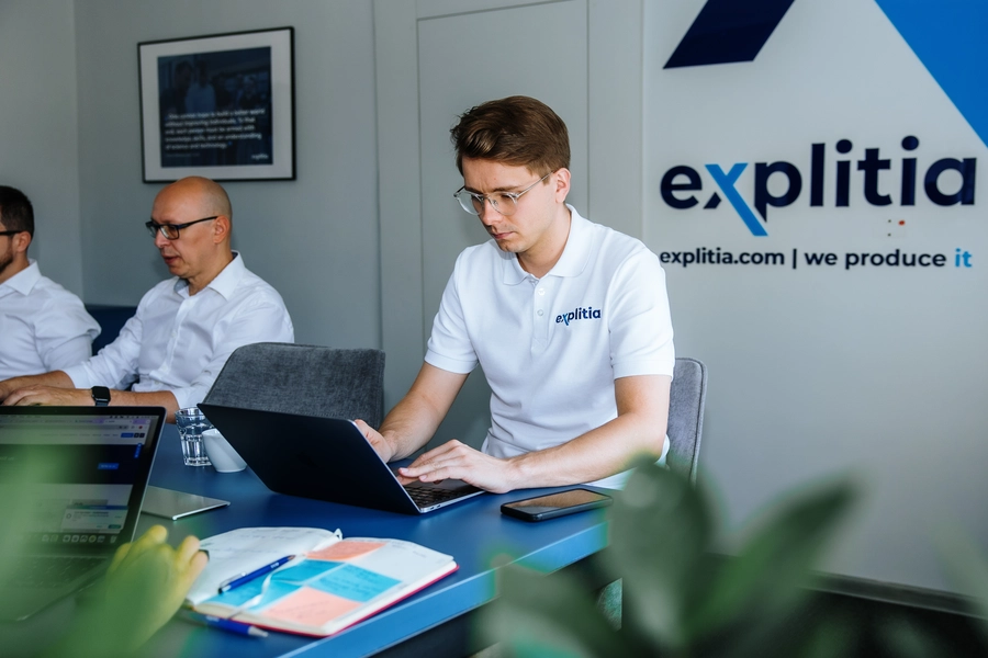 zespół explitia – trzech mężczyzn za stołem, w tle logo explitia