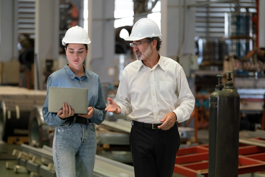 nowoczesne systemy kontroli jakości (kobieta i mężczyzna w białych kaskach wizytują halę produkcyjną)