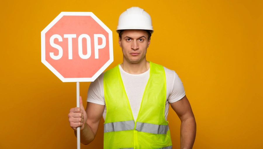 redukcja mikroprzestojów w produkcji (mężczyzna w kasku i kamizelce odblaskowej ze znakiem stop w ręku)