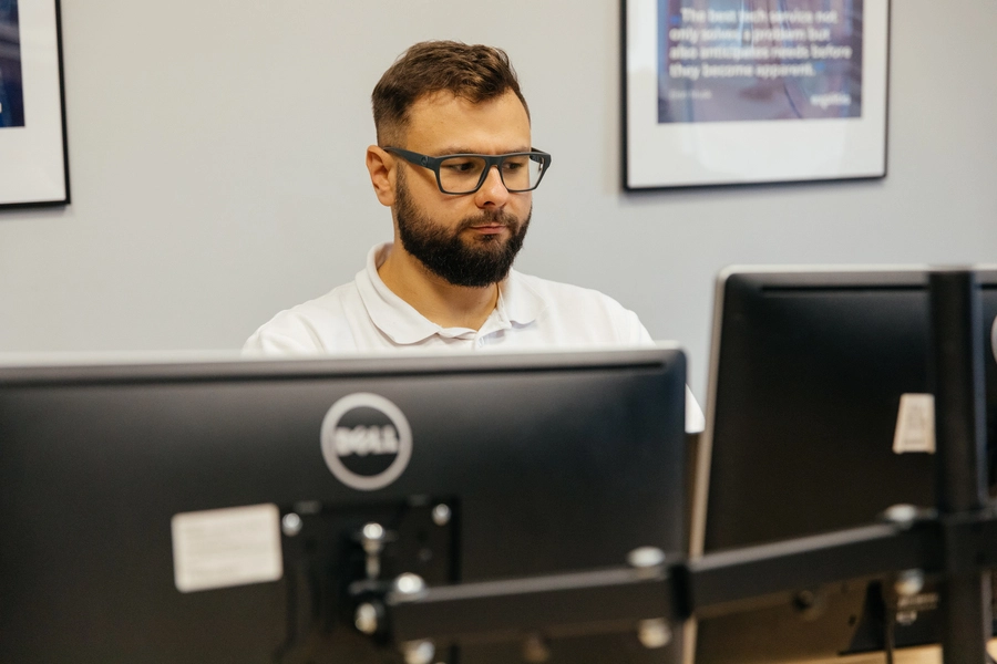 planowanie produkcji w firmie produkcyjnej (programista – mężczyzna w okularach i z zarostem siedzi przed monitorami)